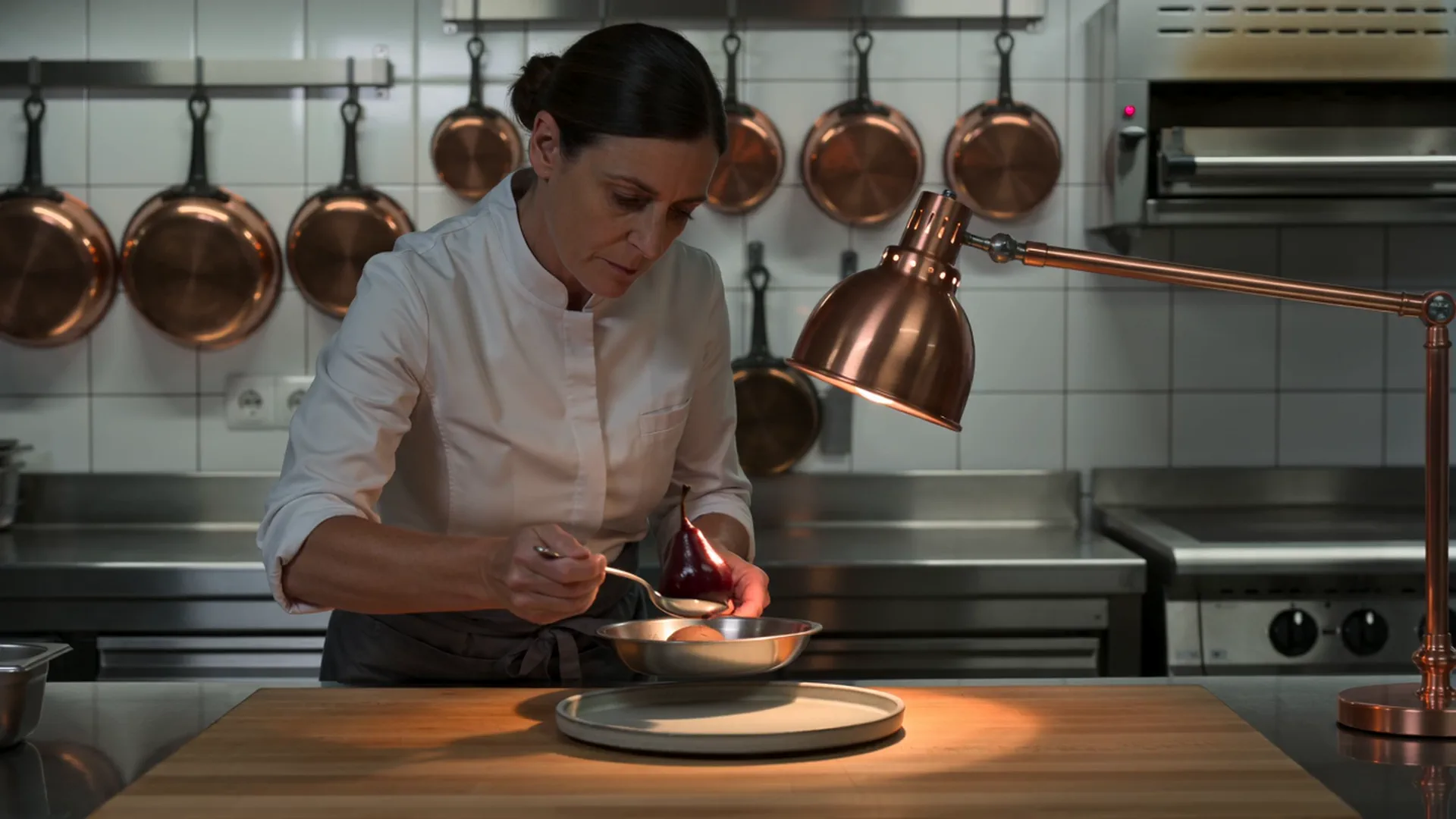 La cheffe dresse une poire pochée au Banyuls sur l&rsquo;assiette, au passe de la cuisine